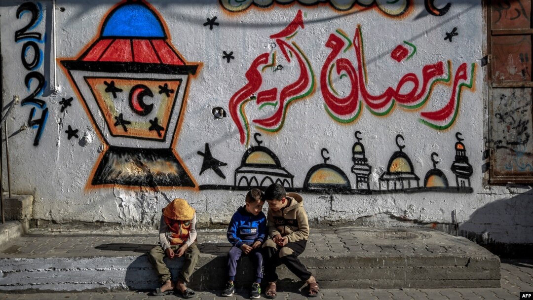 فلسطیني ماشومان په غزه کې د یو دېوال مخې ته ناست دي چې ورباندې د روژې مبارکي لیکل شوې ـ د مارچ اتمې انځور.