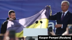 Президент України Володимир Зеленський і президент Литви Гітанас Науседа на площі у Вільнюсі тримають прапор України, який привезли з Бахмута, під час акції на підтримку України у перший день саміту НАТО. Литва. 11 липня. 2023 року