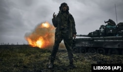 Украинский военный позирует для фото, когда его коллеги ведут огонь из трофейного танка Т-80 по позициям армии РФ в Донецкой области, 22 ноября 2022 года