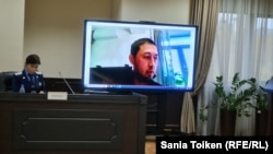 Дистанционно участвующий в суде активист Альнур Ильяшев на экране и прокурор в зале суда. 17 октября 2022 года