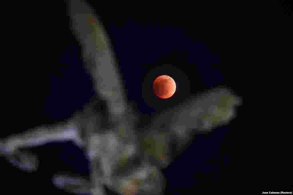 Luna „sângerie” este observată pe cerul din El Salvador, pe 15 mai, 2022. În timpul eclipsei, Pământul continuă să trimită spre Lună o parte din lumina Soarelui, care au o tentă roşiatică în urma unui proces de „refracţie atmosferică".