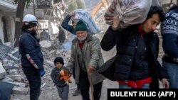 Сирийски мъж с внука си върви сред разрушенията в Антакия. Снимката е от 11 февруари 