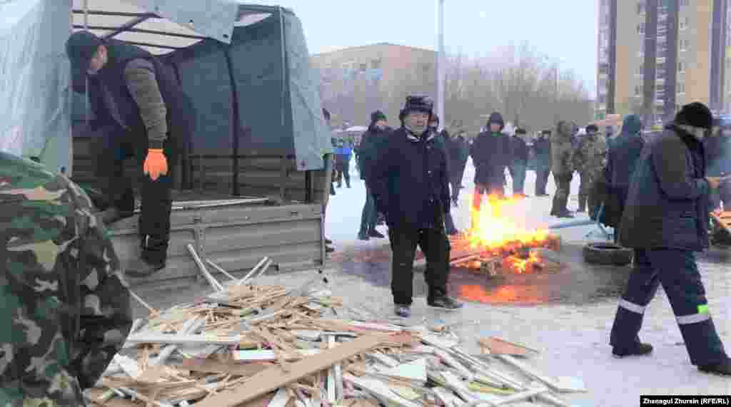 Алаңда тұрған жұрт жылынсын деп от жағу үшін әкелген отынды түсіріп жатқан адамдар. Ақтөбе, 5 қаңтар 2022 ж.