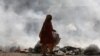 An elderly woman searches for recyclables from a roadside dump in Karachi.