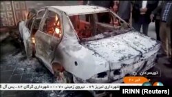 People stand near a burning car in Tuyserkan, Hamadan Province, on December 31.