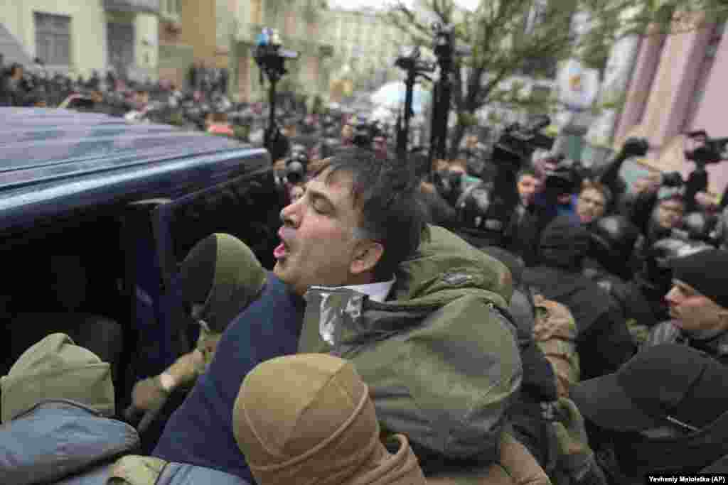 Сотрудники спецназа заталкивают Саакашвили в микроавтобус. Официальной причиной его задержания назвали подозрение в том, что он пытался свергнуть власть в Украине и якобы получал финансирование от людей из окружения свергнутого президента Украины Виктора Януковича. По версии следствия, Саакашвили будто бы «содействовал участникам преступных организаций» и якобы причастен к «сокрытию их деятельности».