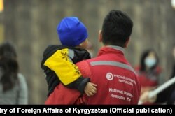 Сотрудник Красного Полумесяца держит на руках ребенка, вернувшегося из Ирака в Кыргызстан