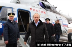 Путин выходит из вертолета на авиабазе Крымск на юге России в январе 2013 года. На заднем плане отдает честь офицер с «ядерным чемоданчиком».