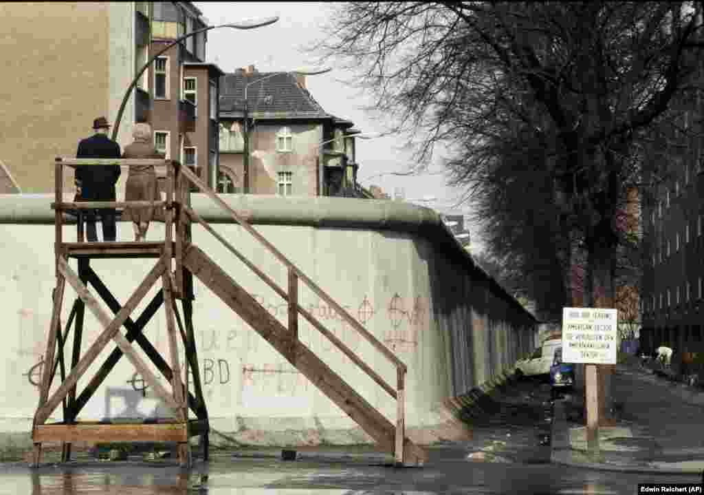 Пара смотрит через стену на Восточный Берлин, снимок сделан в апреле 1983 года. Герхард Зальтер говорит, что испытания противотранспортных заграждений были лишь только частью обширных испытаний и разработок, направленных на то, чтобы не допустить побега из полицейского государства. Сама конструкция Берлинской стены, по его словам, испытывалась «на устойчивость к нападениям с использованием транспортных средств, взрывчатых веществ, а также на выносливость в случае природных катастроф, например, в случае мощных потоков воды во время сильных дождей».