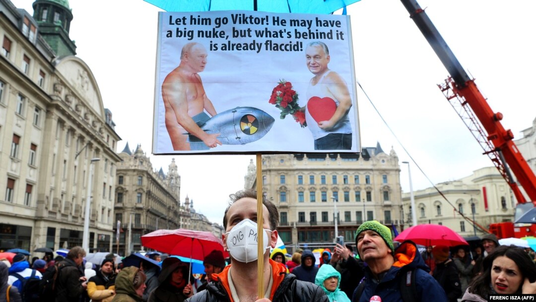 Un manifestant afișează o caricatură cu textul „Lasă-l să plece, Viktor! Poate că are o bombă nucleară mare, dar ceea ce se află în spatele ei este deja flasc!”, în timpul unei manifestații de solidaritate cu Ucraina, la Budapesta, pe 2 aprilie 2022.